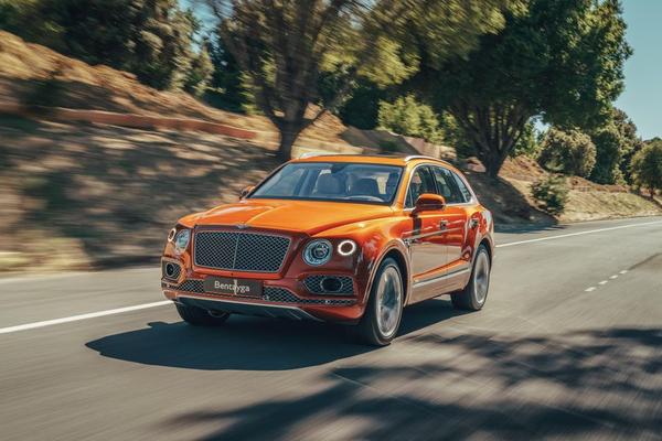 Orange Bentley Bentayga Hybrid driving through trees