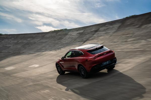 Red Aston Martin DBX driving away from the camera, against a blue sky and smooth concrete road
