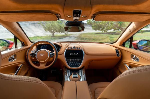 The Aston Martin DBX's tan leather interior, including steering wheel and a view of the forest through the windscreen