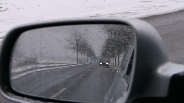 A car seen in a wing mirror, driving on a snowy day