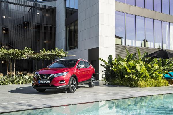 Red Nissan Qashqai lease car parked outside a modern house with swimming pool