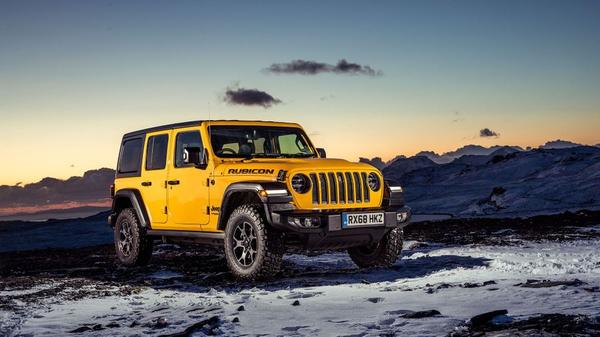 Yellow Jeep Wrangler parked on snowy ground, backed by an early sunrise