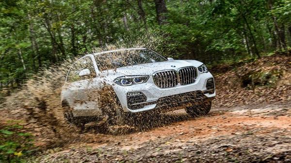 White BMW X5 offroading through a forest and splashing mud