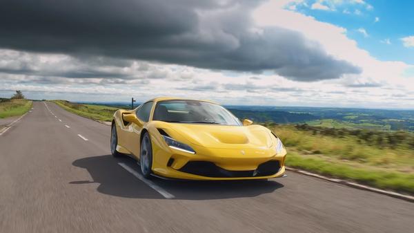 Yellow Ferrari F8 Spider drives down road with heavy cloud behind