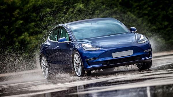 Blue Tesla Model 3 drives through puddles