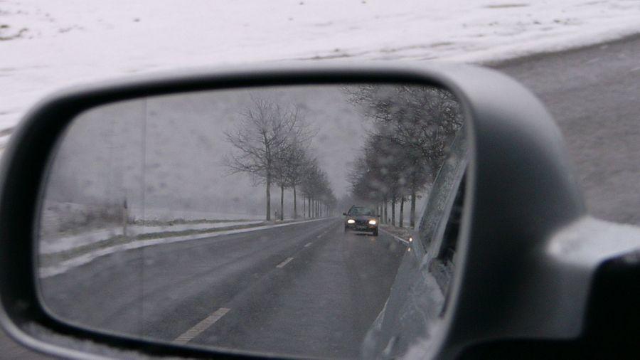 Driving in poor visibility A car seen in a wing mirror, driving on a snowy day
