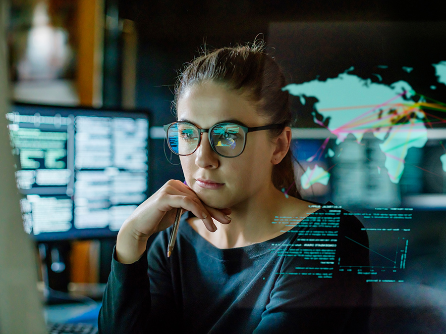 Person analysing global data on a computer screen, with digital maps and code overlays.