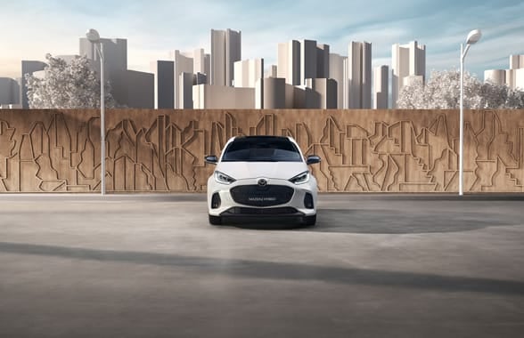 A white Mazda2 with a clean city skyline in the background